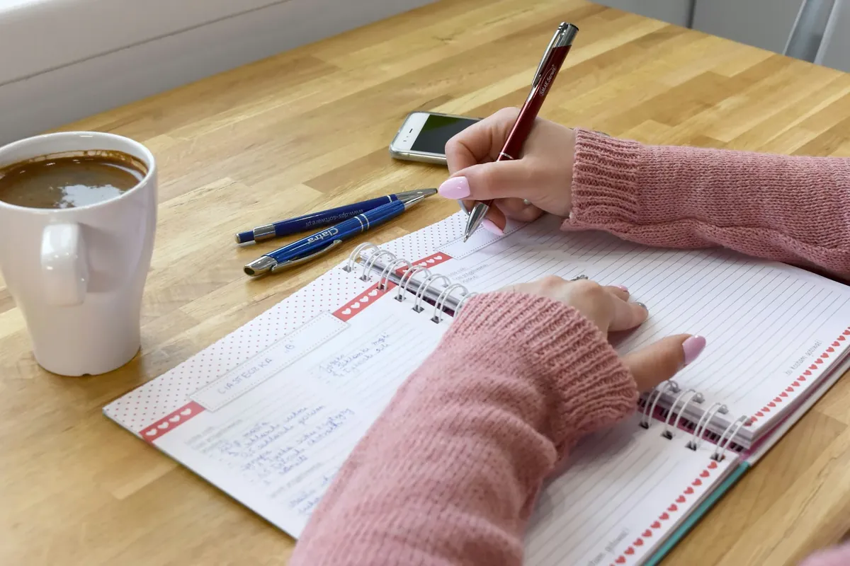 Des mains qui écrivent dans un carnet, un café à côté