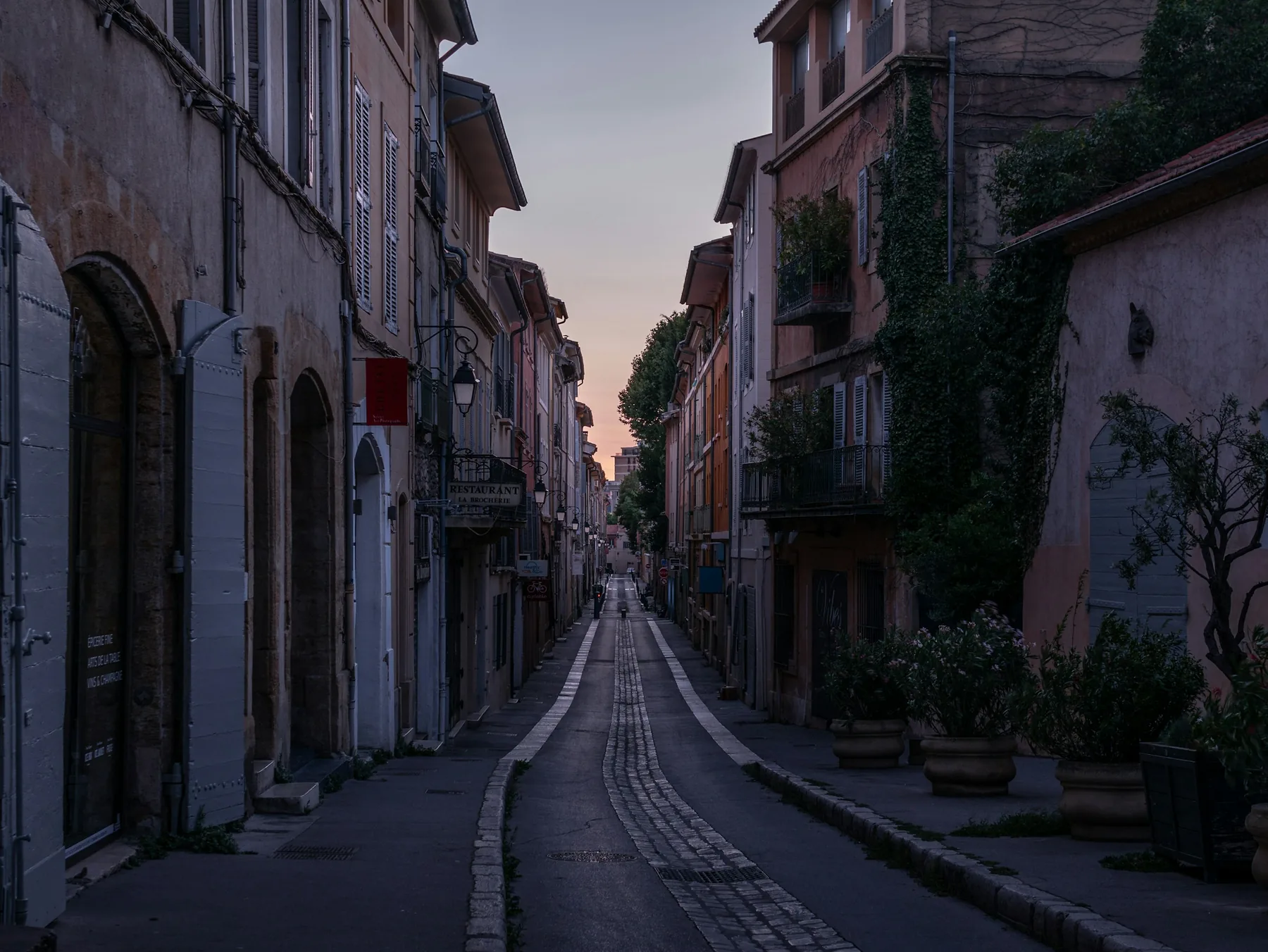 Une rue étroite, des plantes en pot, à la tombée du jour